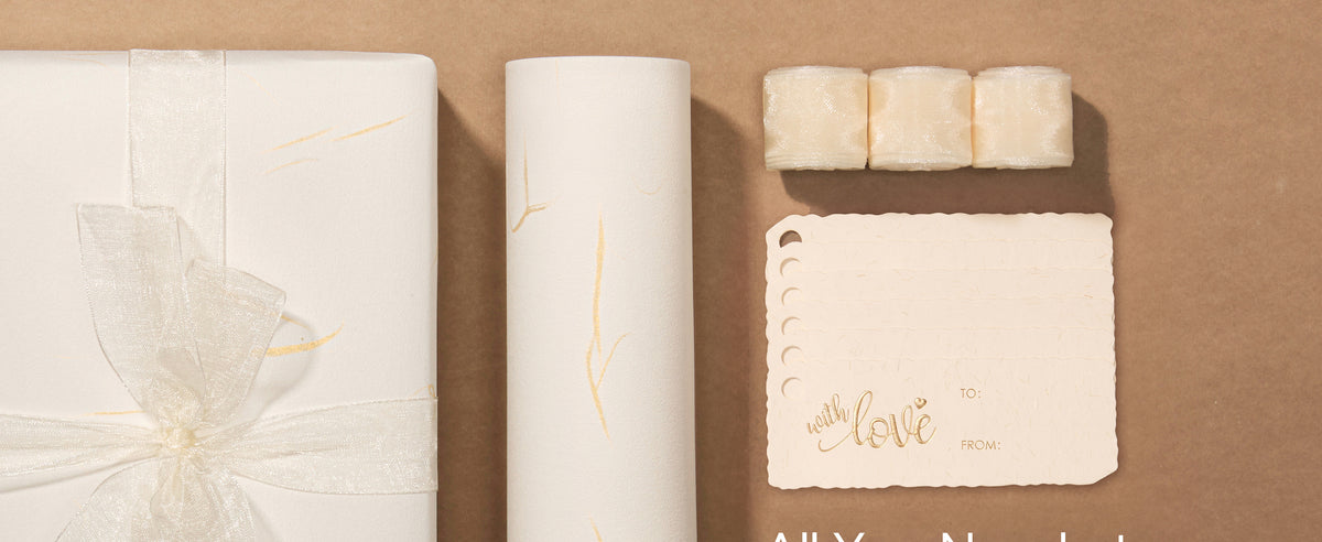 White gold-accented wrapping paper set with sheer ribbon, scalloped tags, and a wrapped gift.