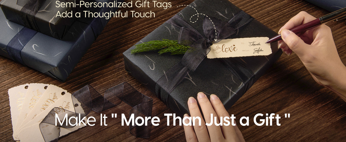 Hands write a gift tag on a black silver-accented package tied with sheer ribbon and evergreen.