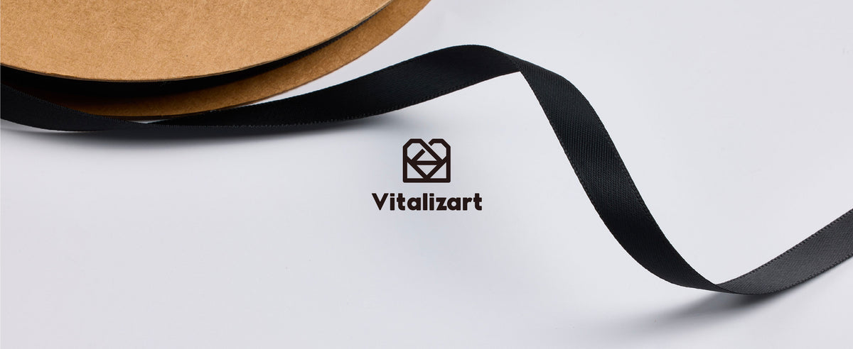 Close-up of smooth black satin ribbon unwinding from a brown cardboard spool with visible woven texture.