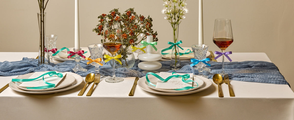 Pastel double-faced satin ribbon set arranged across a styled dining table with gifts and floral accents
