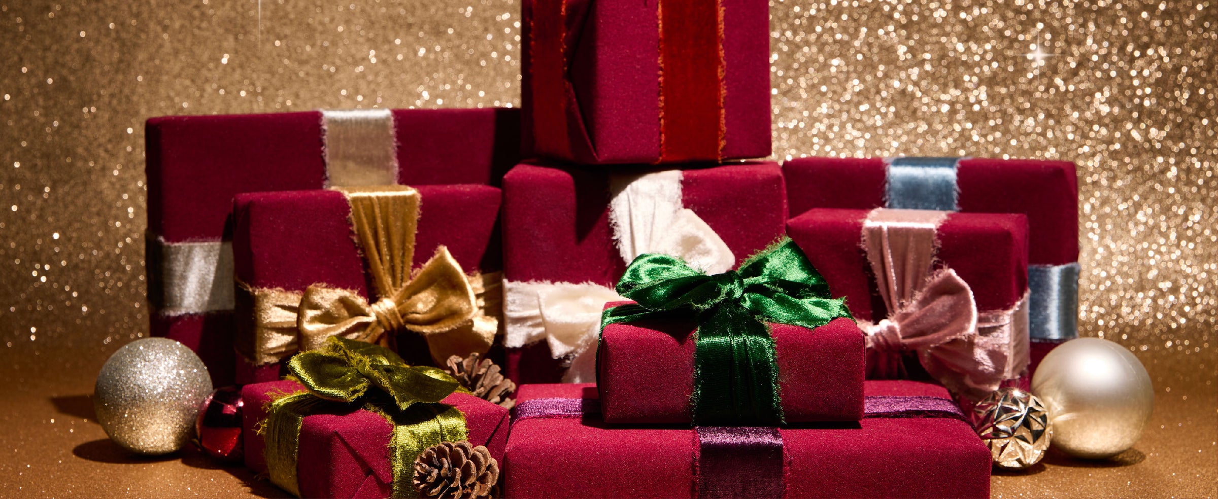 Holiday gifts wrapped in red velvet and tied with colorful ribbons, including an emerald green bow
