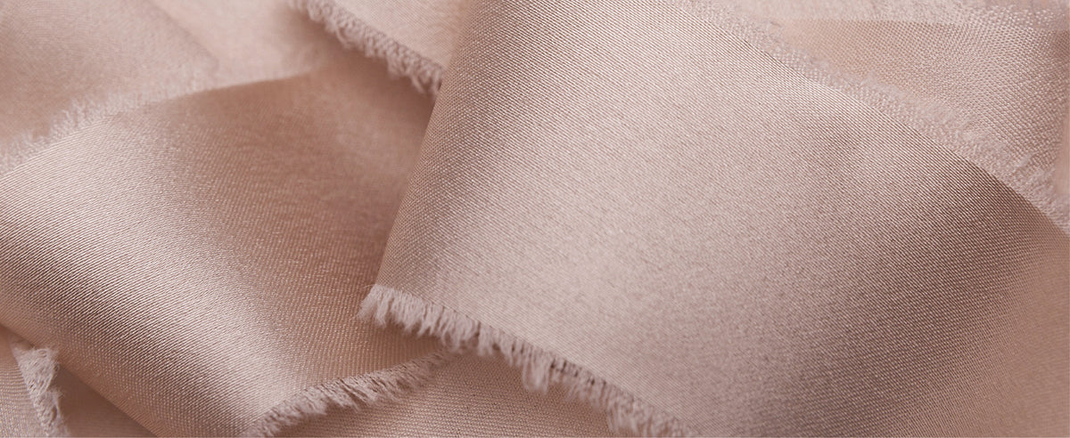 Close-up of nude-pink satin ribbon in soft waves, showing its smooth sheen and wispy frayed edges.