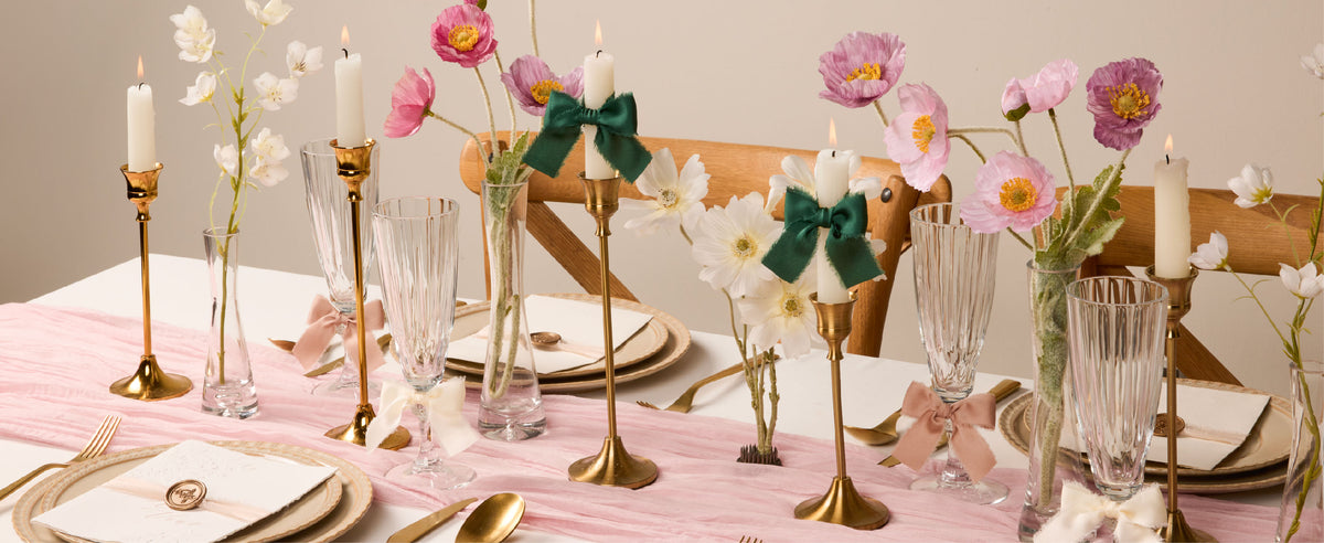 Dark green satin ribbon bows decorate candles on a floral table set with gold accents