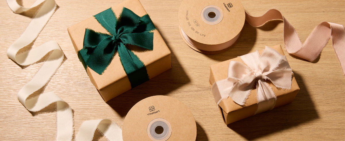 Kraft gift boxes tied with dark green and pale blush frayed satin ribbon beside 30-yard spools