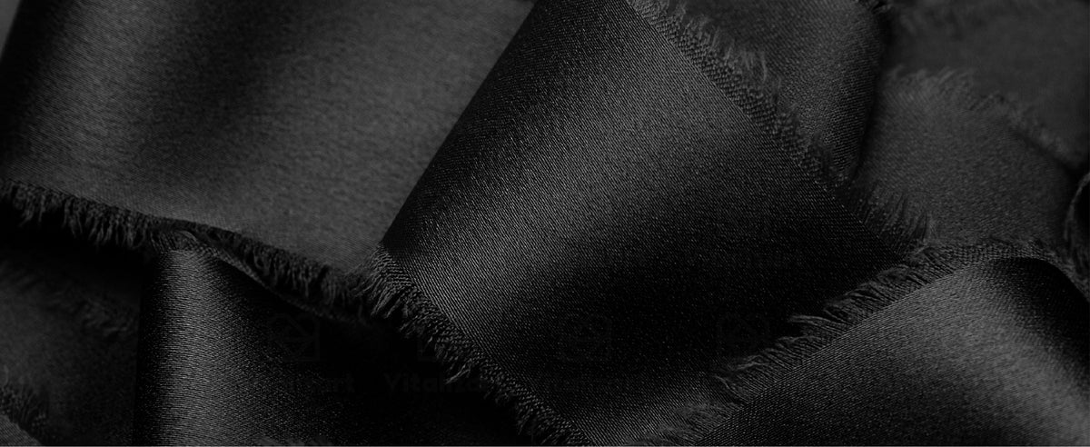 Close-up of black satin ribbon with soft frayed edges, layered in glossy folds and loose loops.