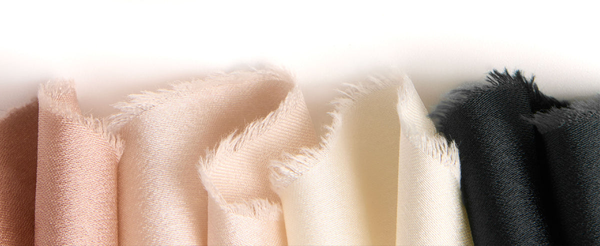 Black, ivory, blush, and pale pink satin ribbons with frayed edges framing a blank white center.