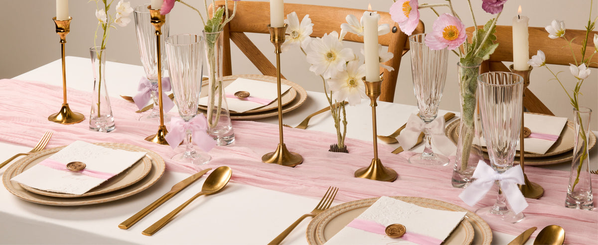 Pink and nude frayed satin bows decorate crystal glasses in a candlelit floral table setting.