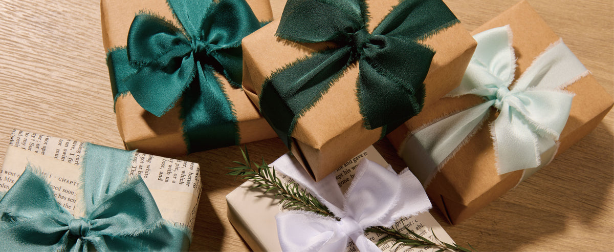Kraft and white gifts tied with dark green, teal, sage, and white frayed satin ribbon bows.