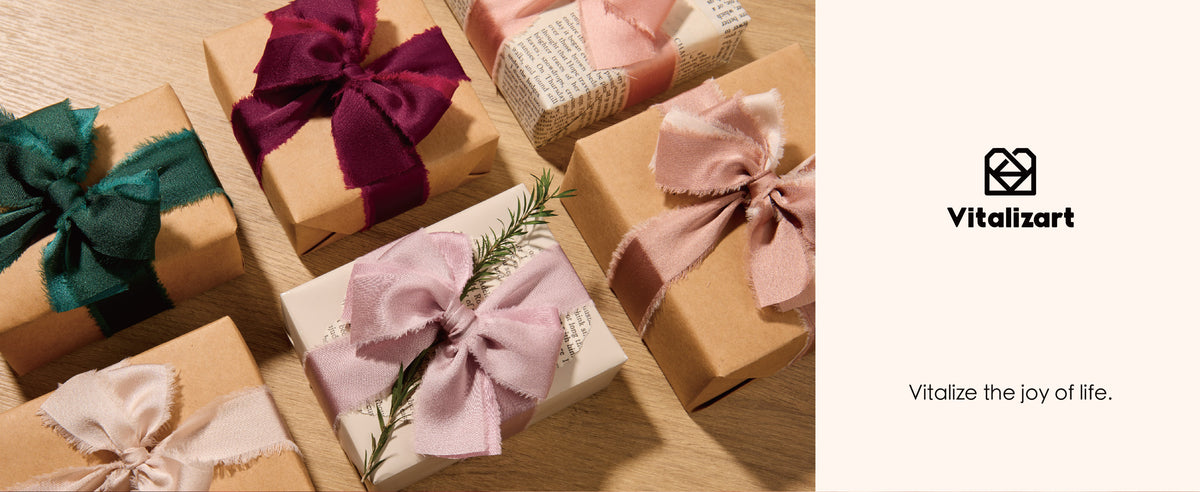 Gift boxes tied with burgundy, teal, blush, and lavender frayed satin ribbon bows on a wood table.
