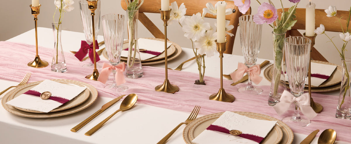 Frayed burgundy and pink satin ribbon accents on glasses and invitations at a floral table setting.