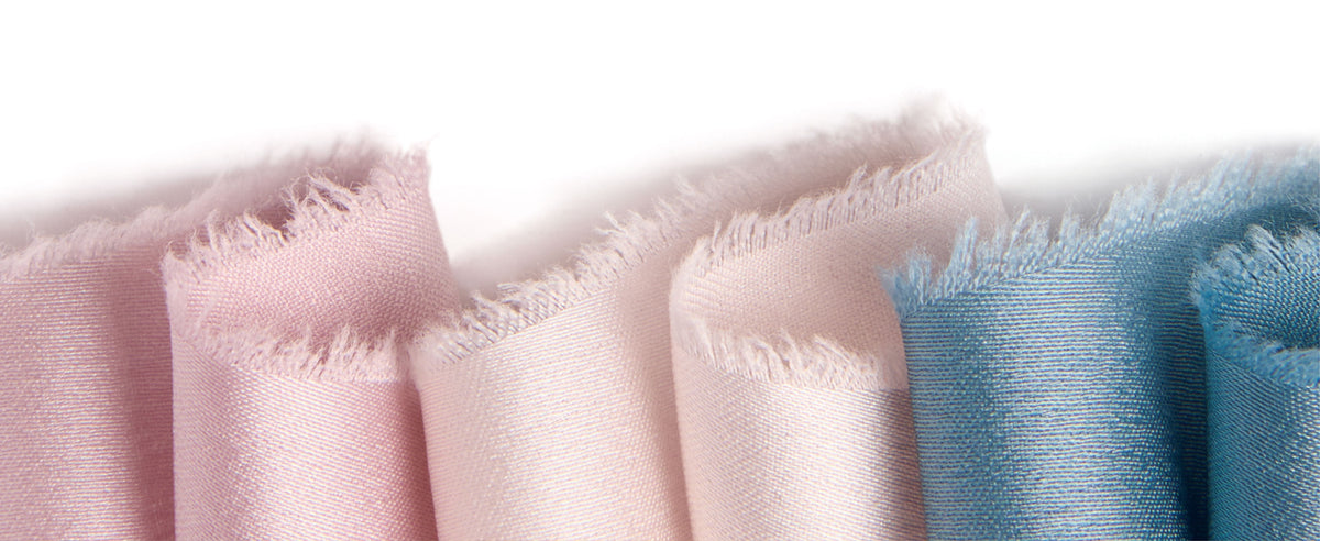 Macro view of blush, pale pink, and blue satin ribbons showing fine weave and soft frayed edges.