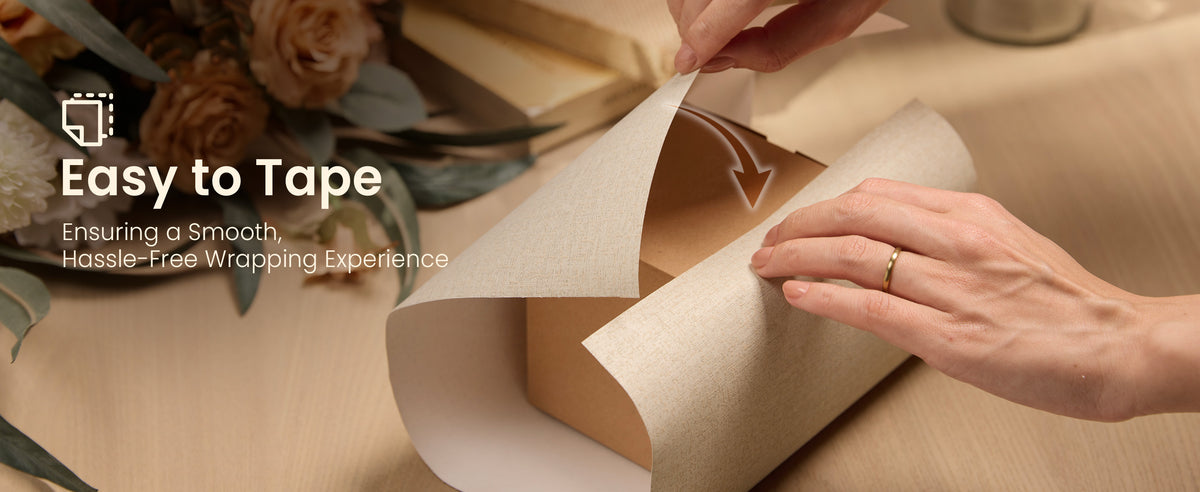 Hands folding beige linen-textured wrapping paper over a rectangular gift box