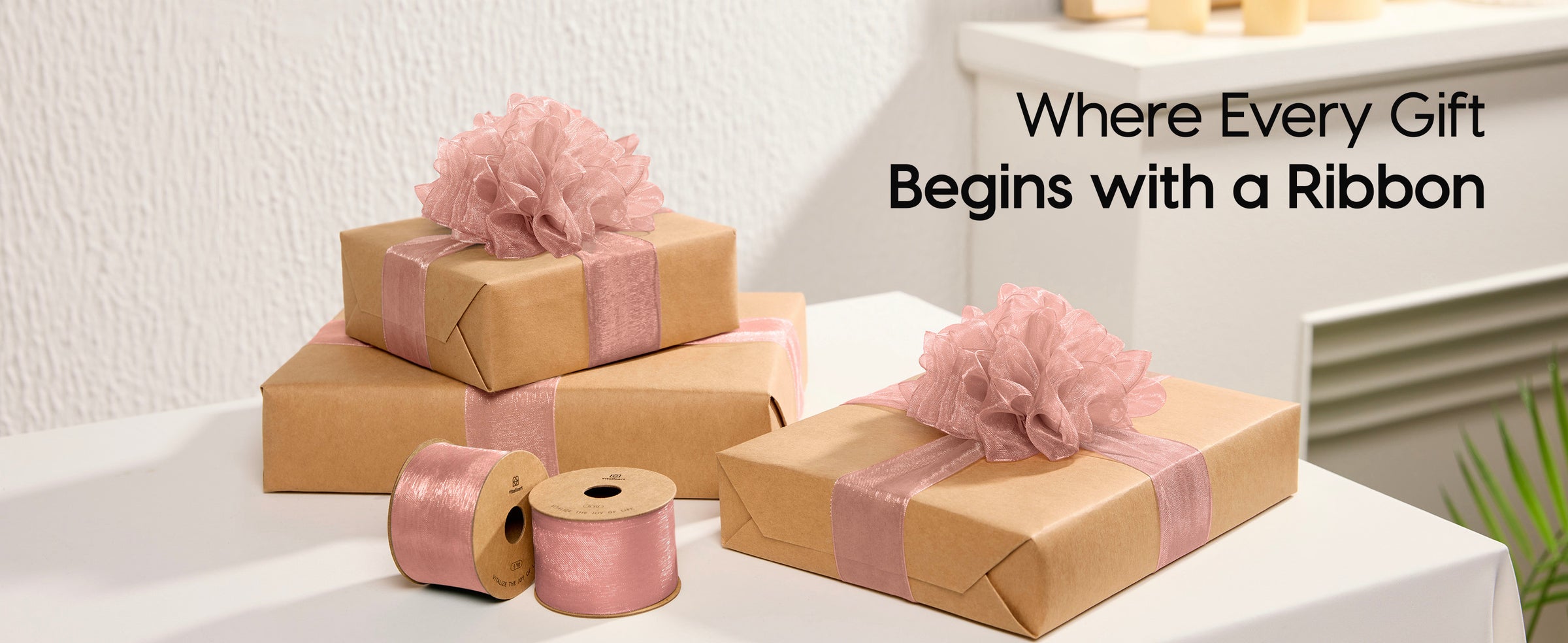 Kraft-paper gifts decorated with dusty rose organza ribbon and large layered bows beside two spools