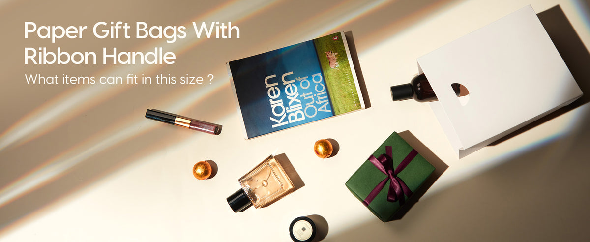White small paper gift bags with ribbon handles styled beside cards, gifts, and small accessories