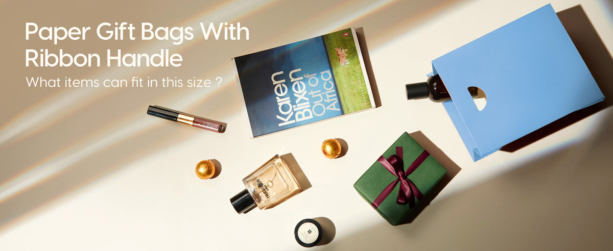 Open blue paper gift bag beside a book, perfume, cosmetics, small jar, bottle, and wrapped gift