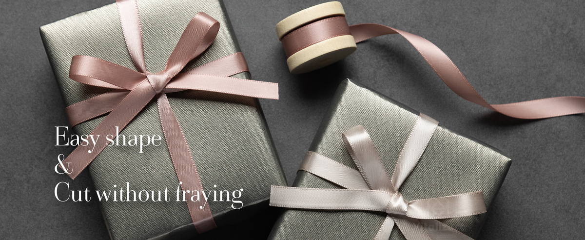 Dusty pink and pale beige satin ribbons form bows on two gray gift boxes beside wooden spools.