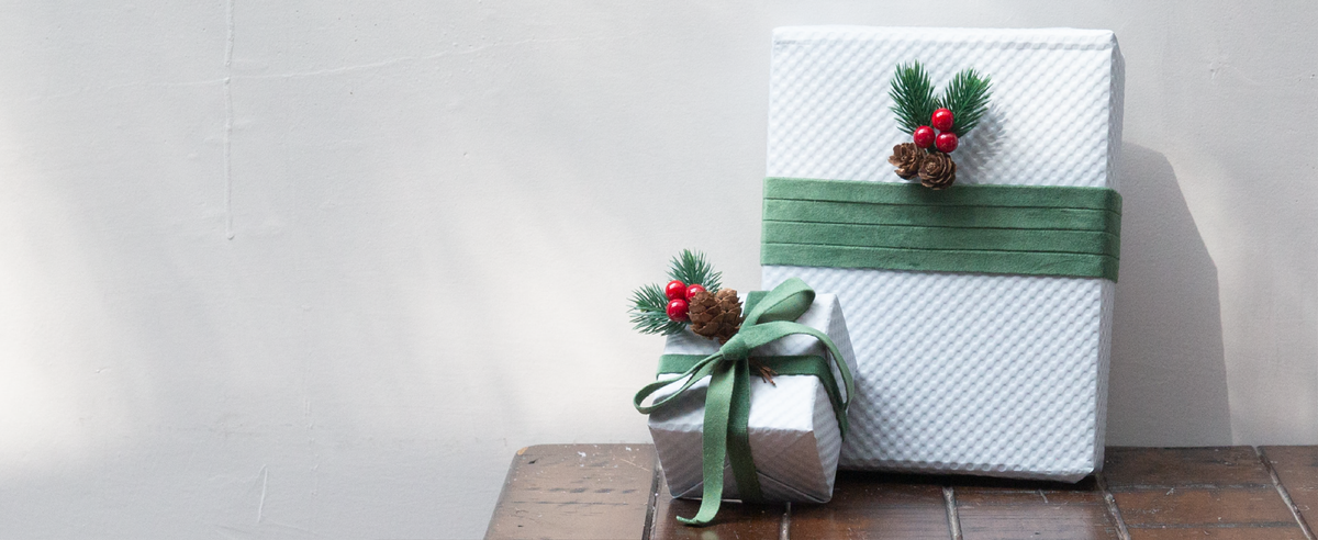 White holiday gifts wrapped with green velvet ribbon, pinecones, evergreen sprigs, and red berries.