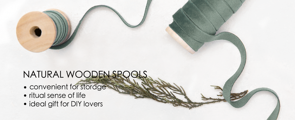 Dusty green velvet ribbon wound on natural wooden spools, with a loose strand and dried greenery.