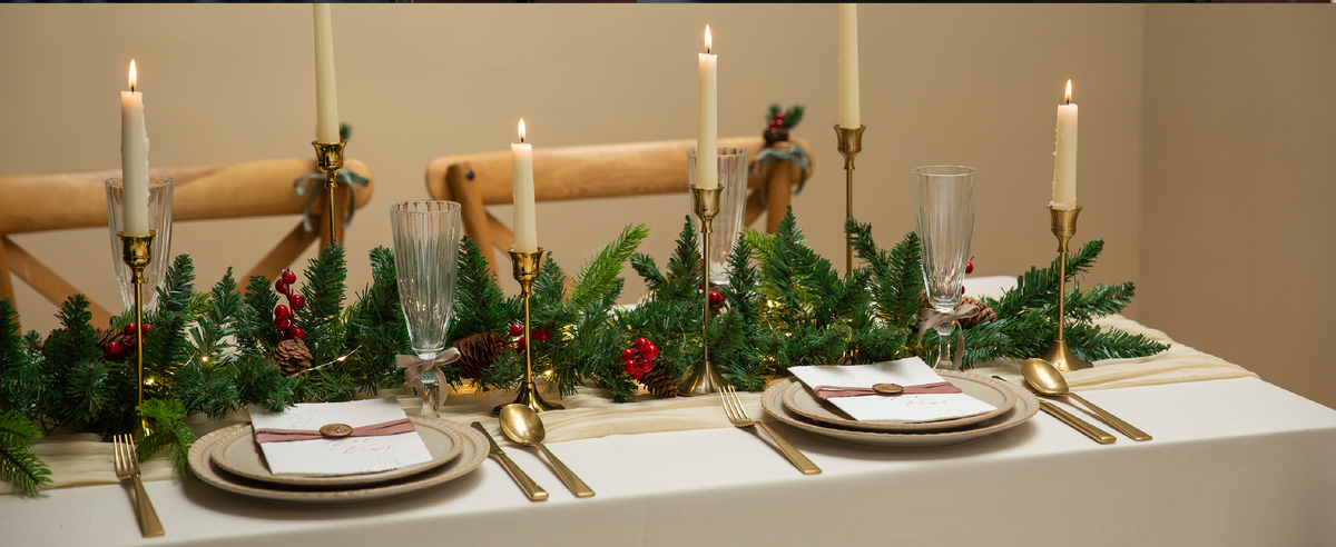 Red and green velvet ribbon set styled across a dining table with flowers, candles, and place settings