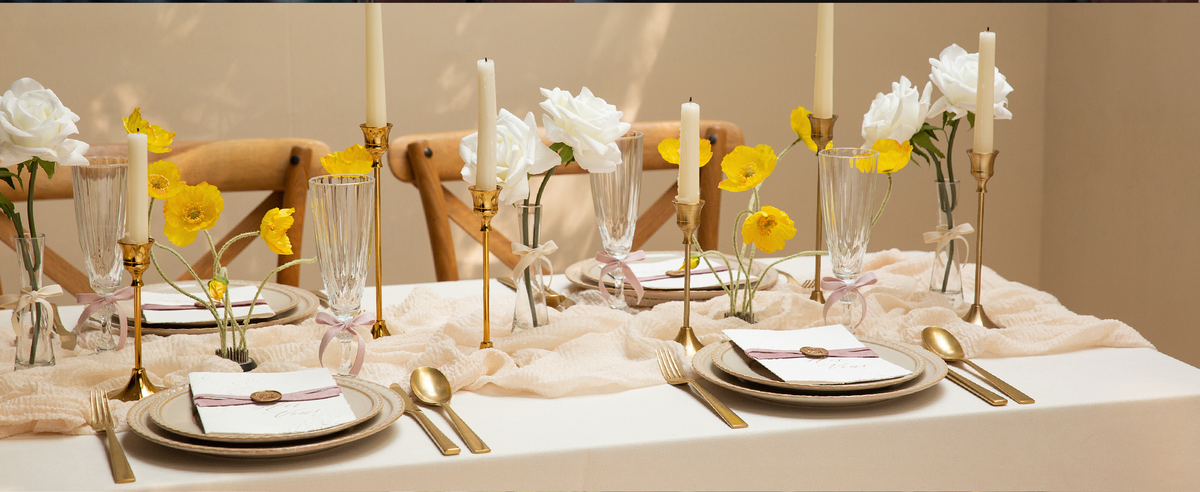 Pale pink velvet ribbon accents glass stems, flower vases, and invitations on an elegant wedding table.
