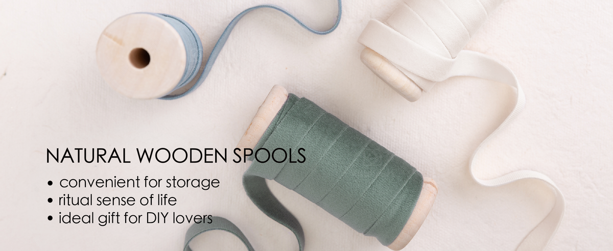 Blue-gray, sage green, and white velvet ribbon wound on natural wooden spools with loose trailing ends.