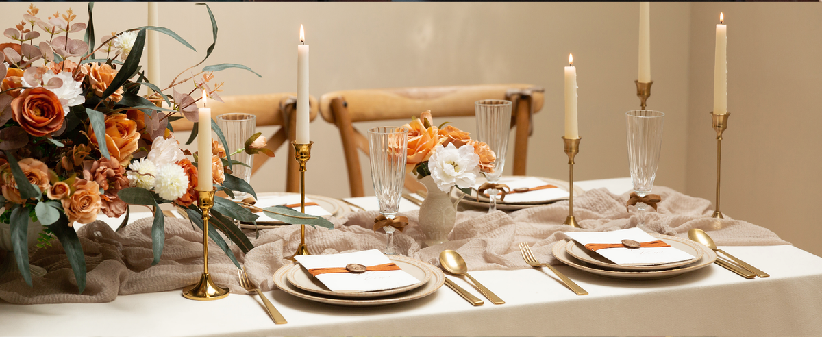 Brown and burnt orange velvet ribbon accents glass stems and invitations on a candlelit dining table.
