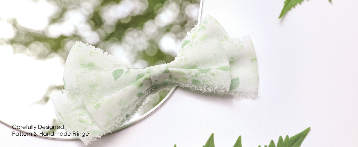 Green leaf-print frayed ribbon tied around a blush bouquet and a white chair arrangement