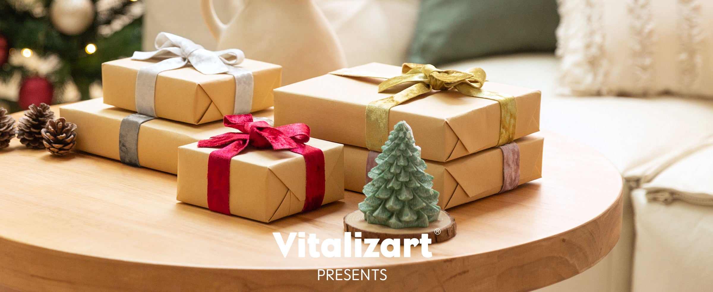 Kraft gift boxes tied with velvet ribbons, including a deep red bow, arranged beside a Christmas tree