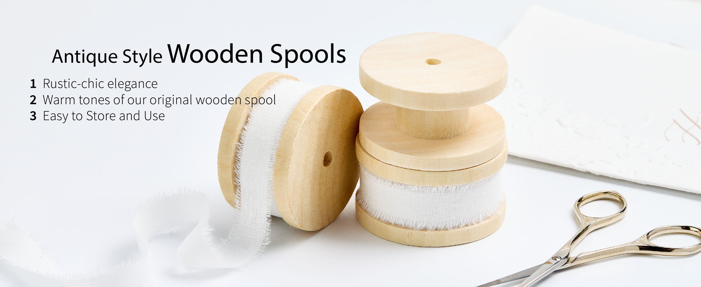 White frayed cotton ribbon on three pale wooden spools with loose ribbon and gold craft scissors