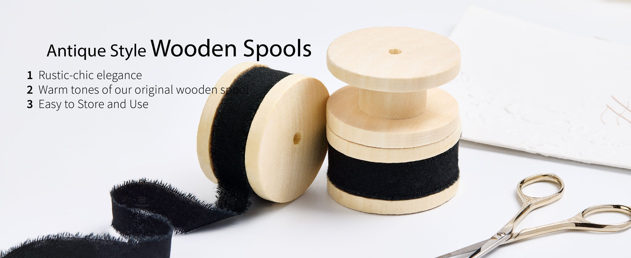 Black frayed cotton ribbon on three pale wooden spools with loose ribbon and gold craft scissors
