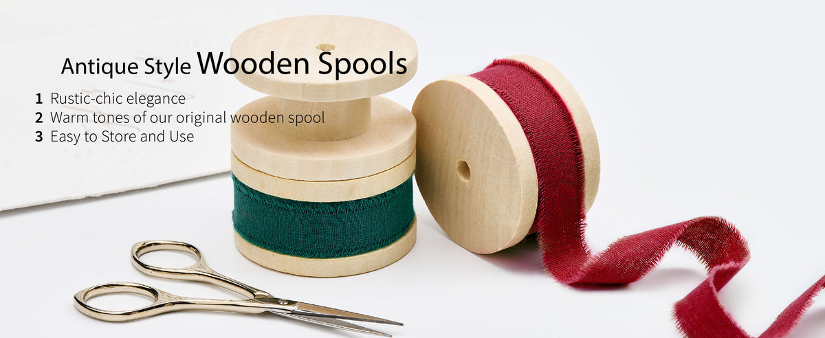 Green and deep red frayed cotton ribbon on light wooden spools beside small gold scissors