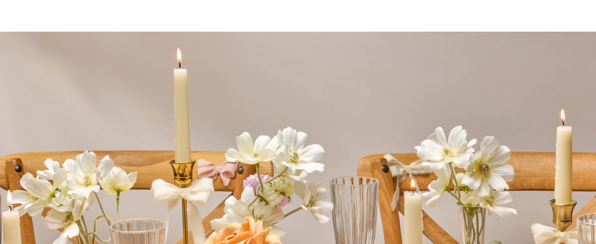 Pale pink fringed cotton ribbon tied in bows around a flower vase and a textured invitation.