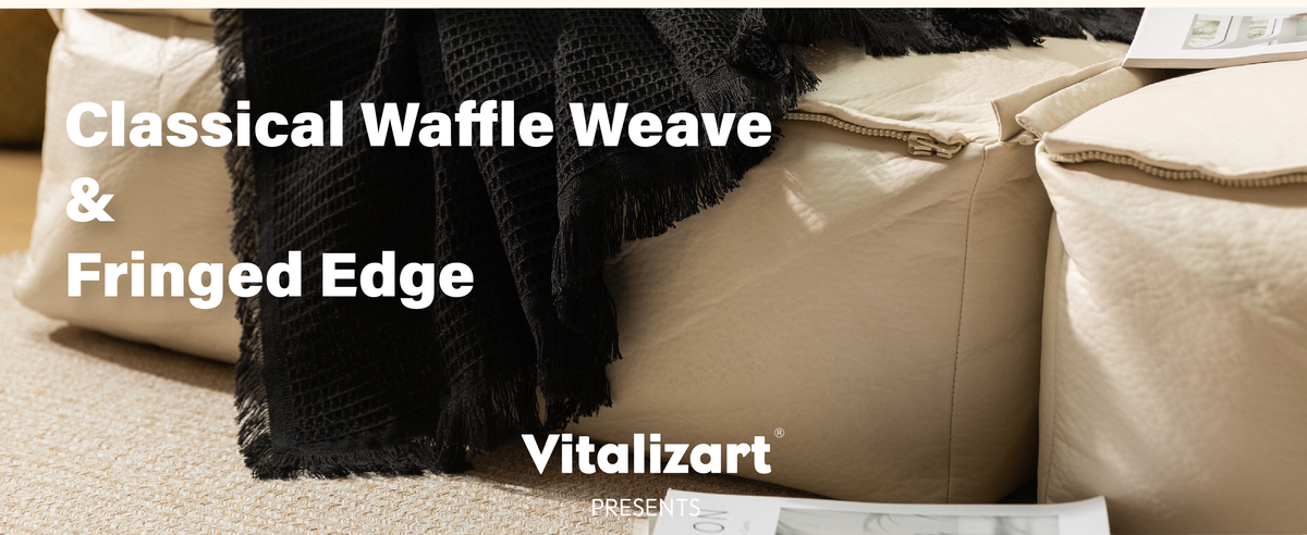 Black waffle-weave throw blanket with fringed edges draped over a beige sofa