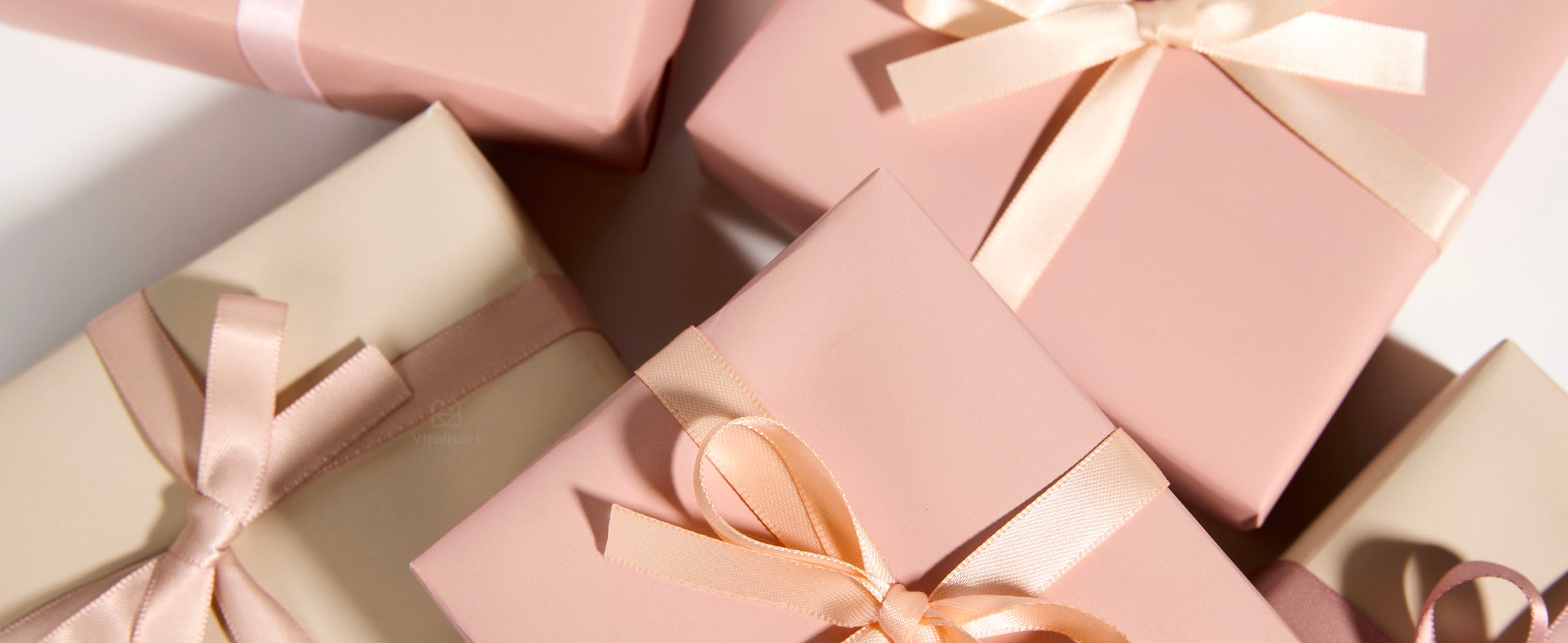 Pink and cream gift boxes tied with narrow satin bows in blush, peach, cream, and dusty mauve.