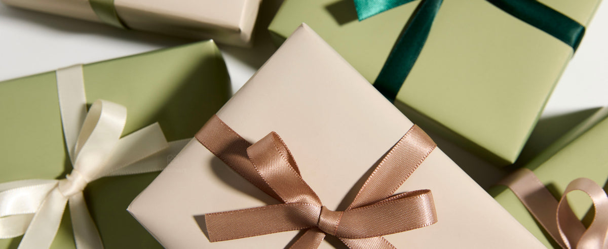Cream and pale green gift boxes tied with glossy teal, sage, ivory, and blush satin bows.