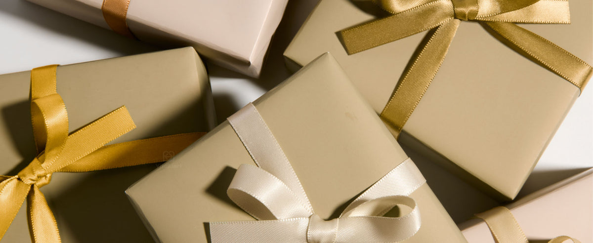 Kraft satin ribbon boxes and flat cardboard packaging pieces arranged on a sunlit wooden table