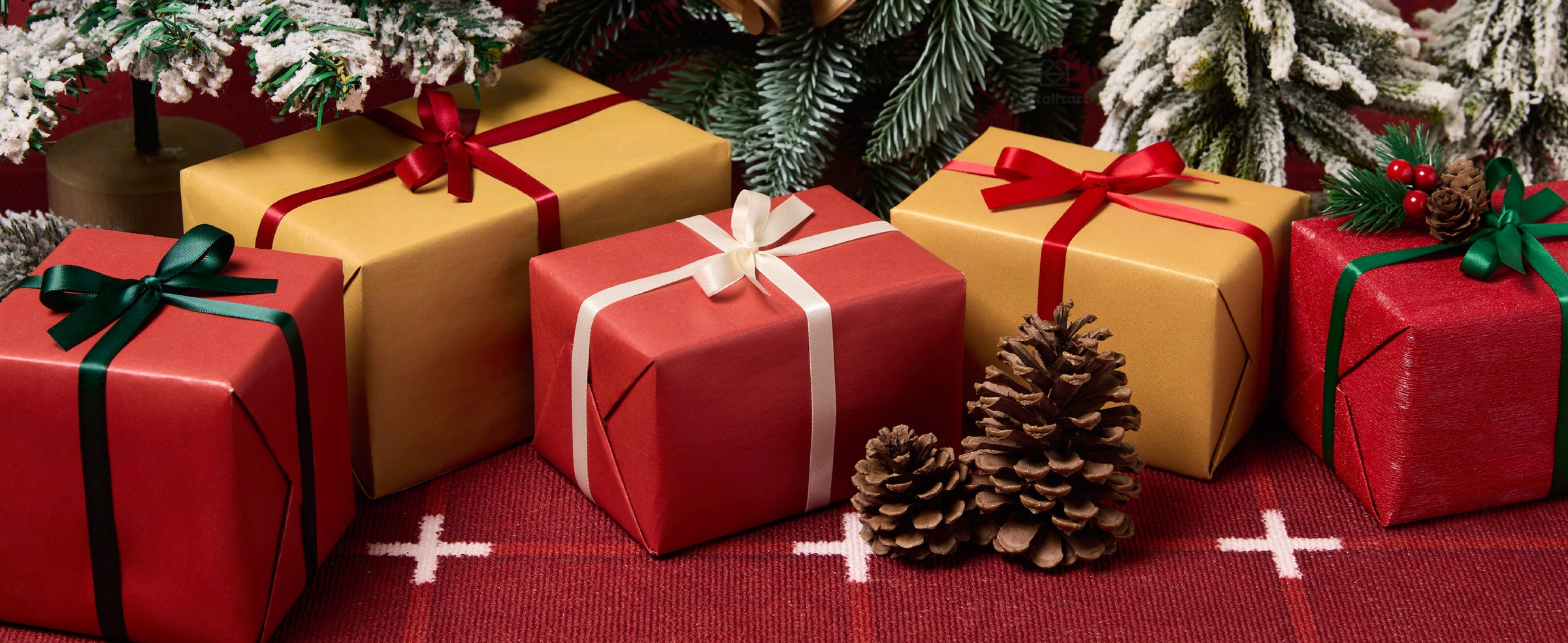 Christmas gifts tied with red, cream, green, and teal satin ribbons beneath snowy evergreen branches.