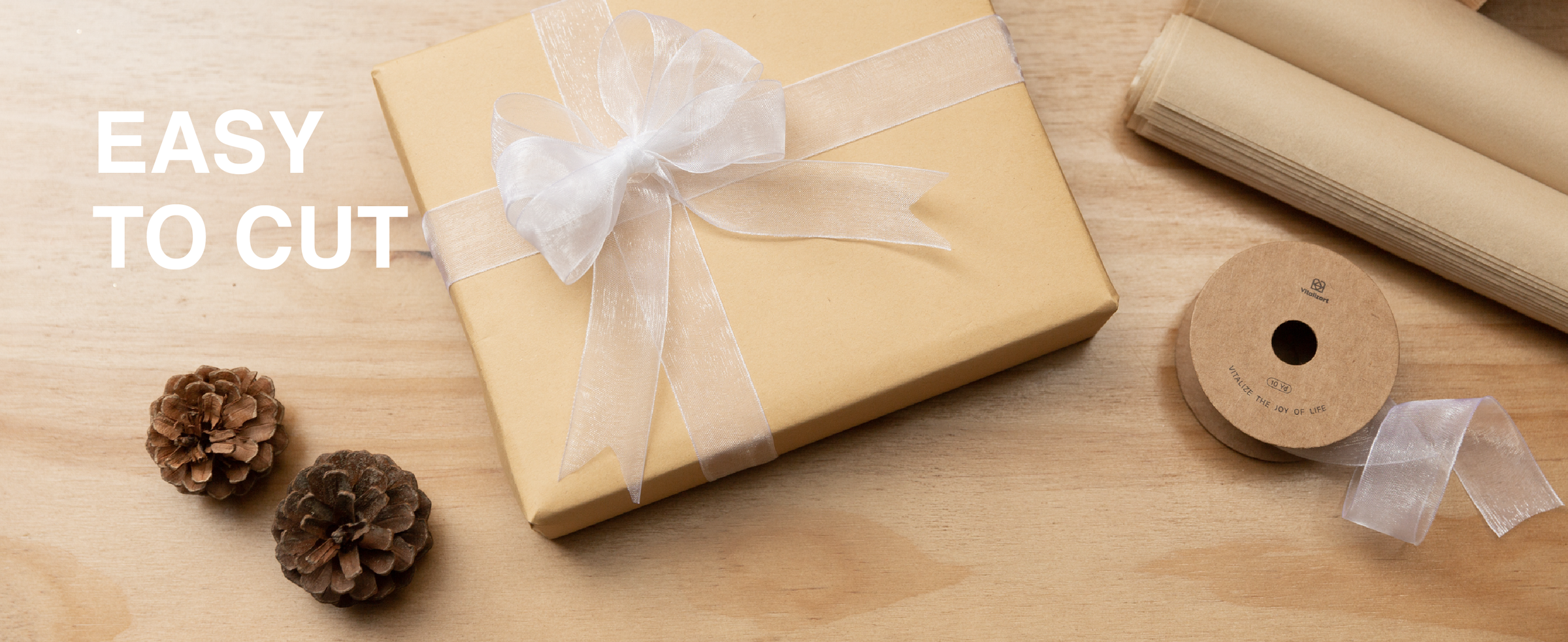 White sheer ribbon tied in a bow around a kraft gift box beside scissors and a spool