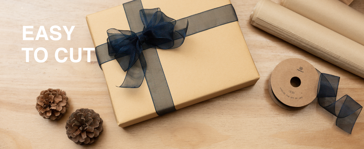 Navy-blue sheer organza ribbon tied around a kraft gift box beside scissors and a matching spool.