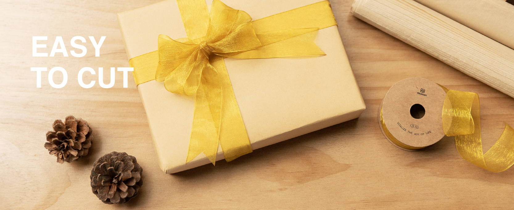 Gold sheer organza ribbon tied around a kraft gift box beside scissors and a matching spool.