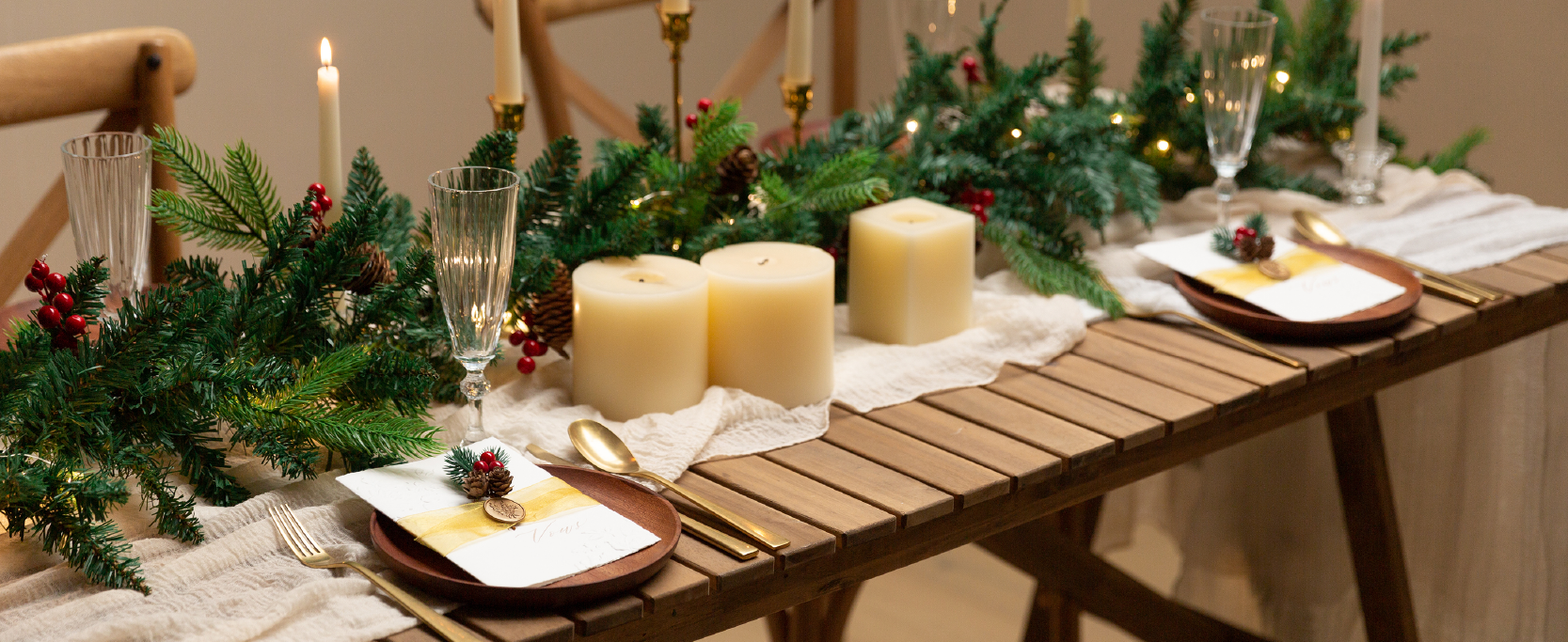 Sheer gold organza ribbon accents place cards on a candlelit Christmas table with evergreen garland.