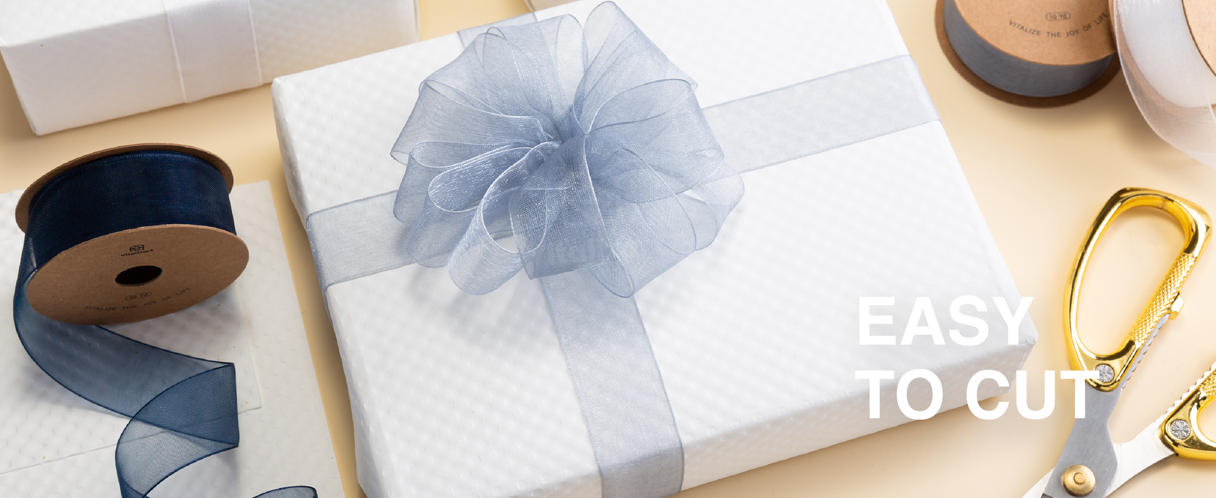 Blue-gray organza ribbon tied in a large bow around a white gift box beside spools and scissors