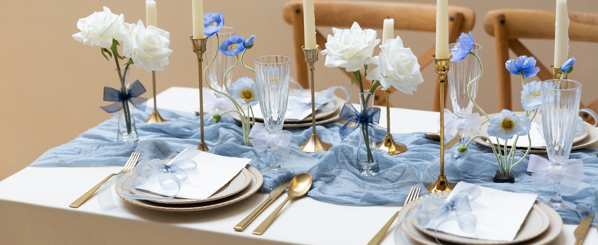 Blue and white sheer ribbon bows decorate flowers, glasses, and place settings on a formal dining table