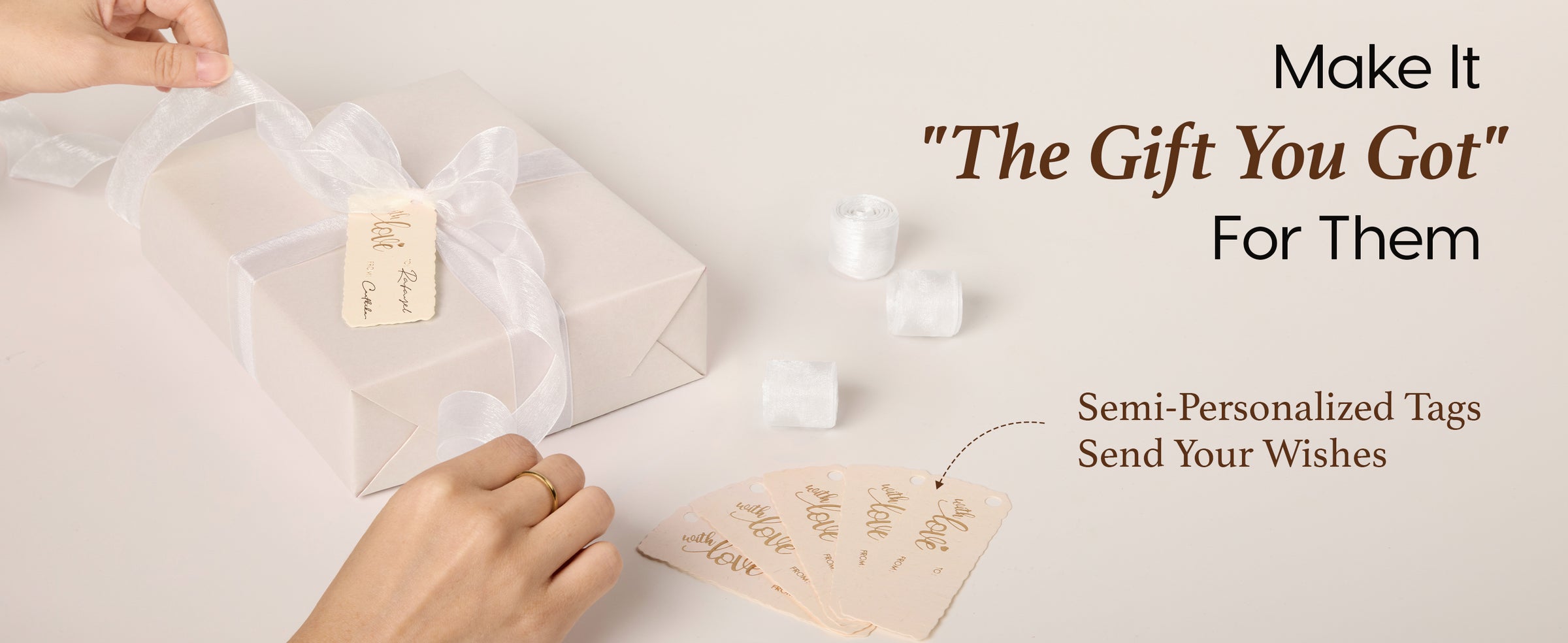 Hands tie white organza ribbon on a pearly wrapped gift with writable cream tags