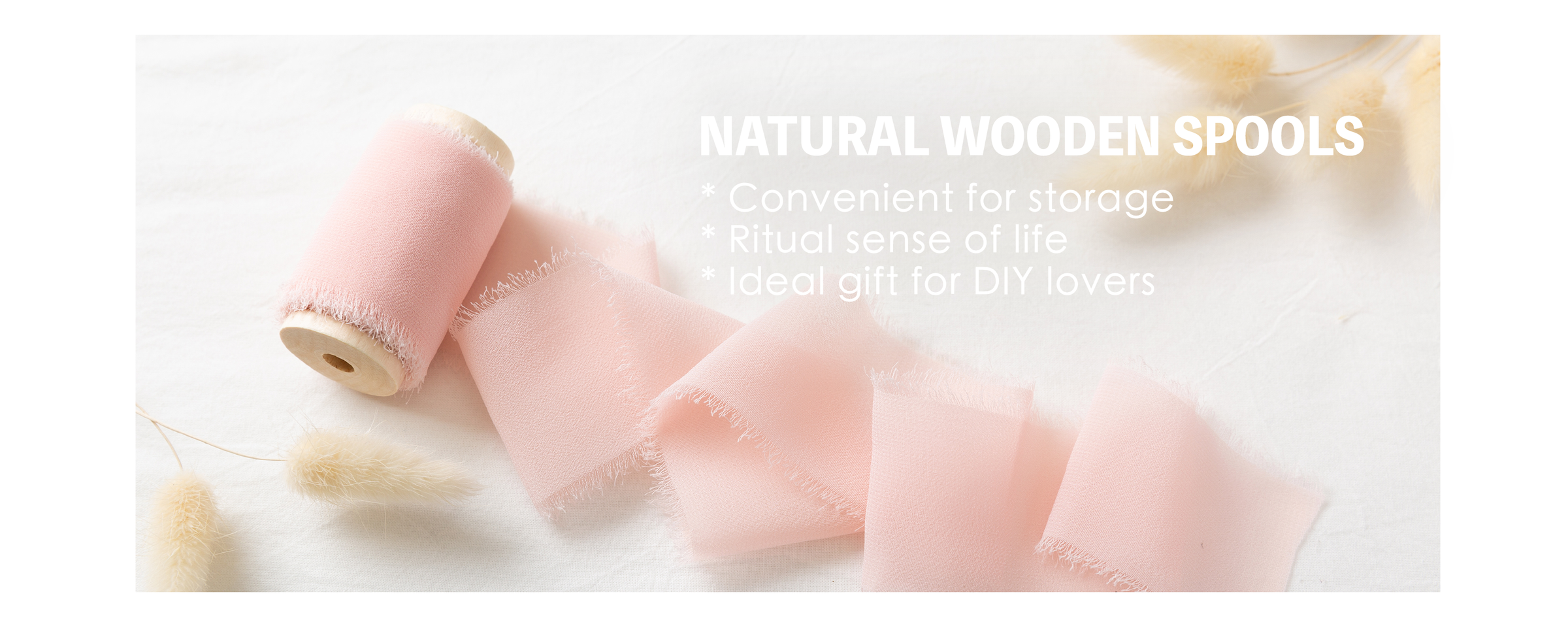 Pale pink chiffon ribbon with feathered edges unrolling from a natural wooden spool on white fabric.