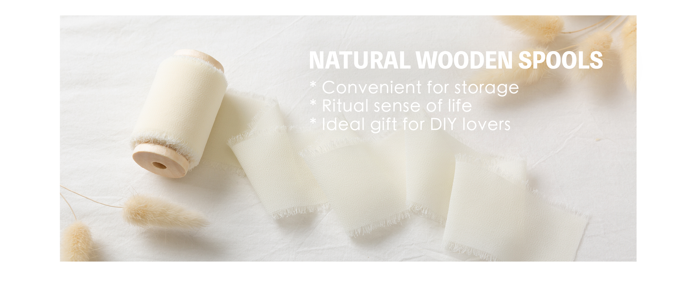 Cream white chiffon ribbon unfurled from a natural wooden spool beside dried grasses
