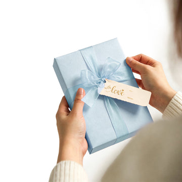 Hands holding a blue gift wrapped with organza ribbon and a With Love tag