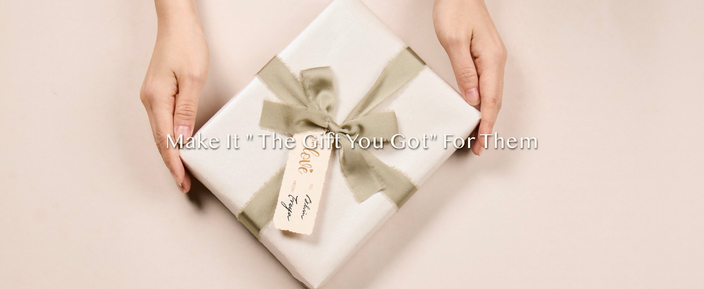 Hands presenting a pearly white gift finished with a sage ribbon bow and cream tag
