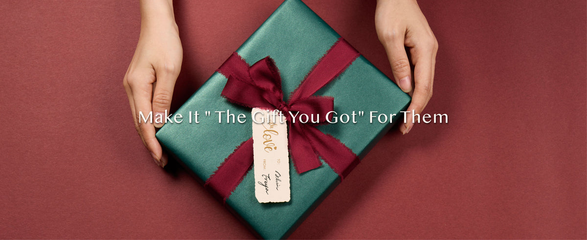 Hands presenting a pearly green gift finished with a burgundy ribbon bow and cream tag