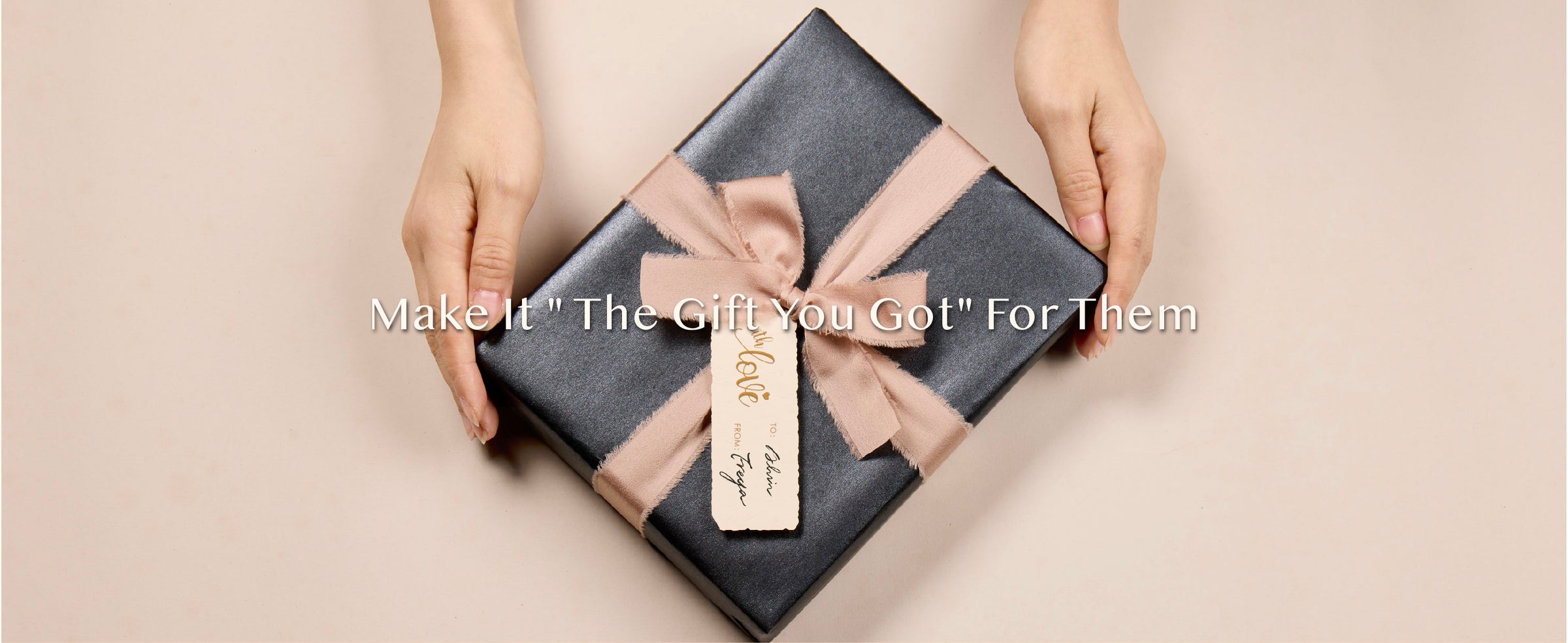 Hands presenting a dark pearly gift wrapped with a wide nude ribbon bow and cream tag